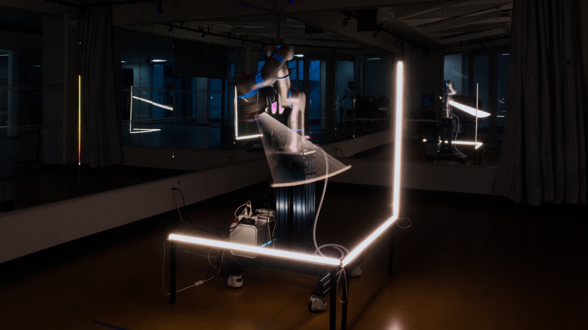 Long-exposure photograph of a robot arm holding a light tube, tracing motion trails above a glowing rectangular frame on the studio floor