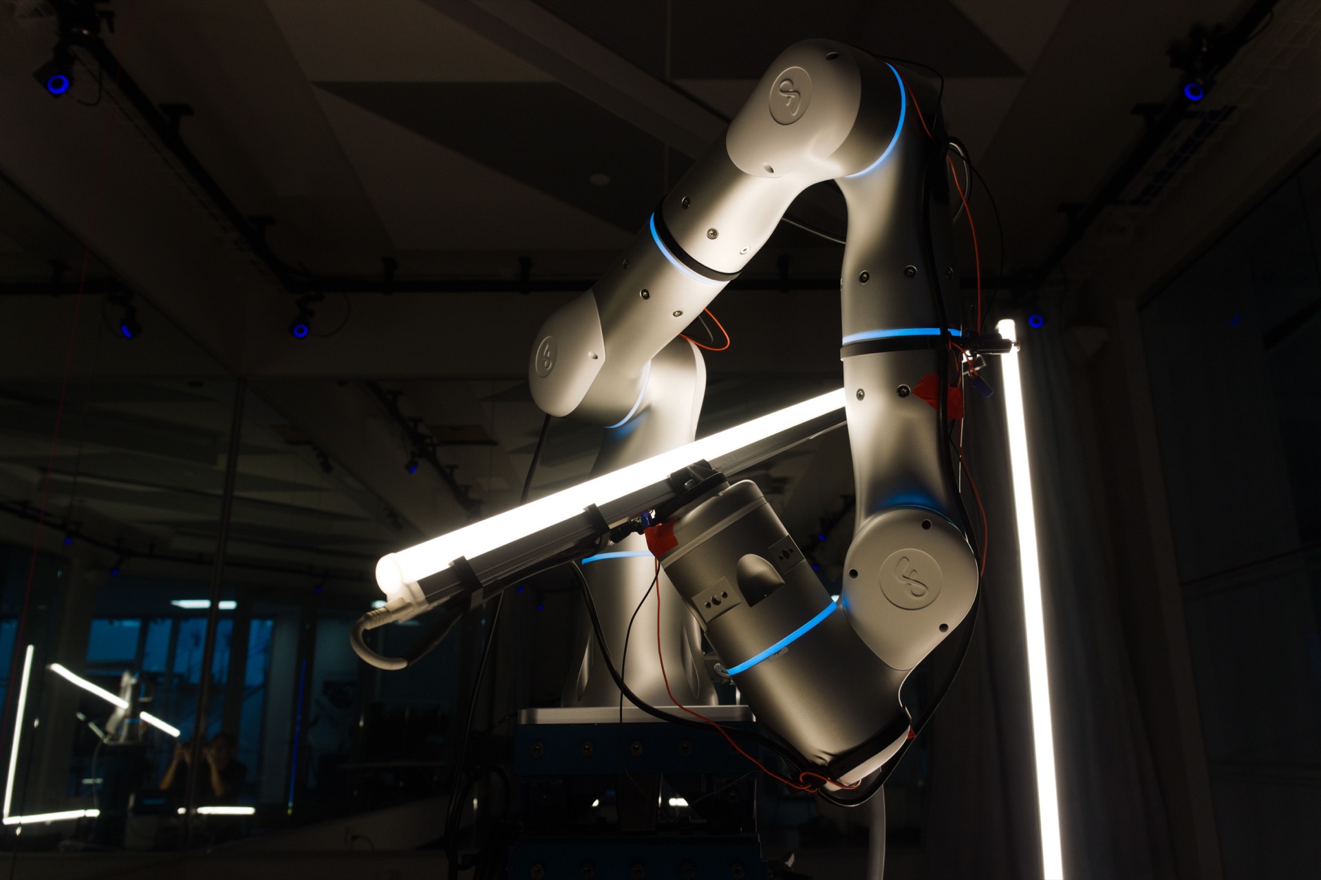 Close-up of the robot arm gripping a light tube in a dark studio