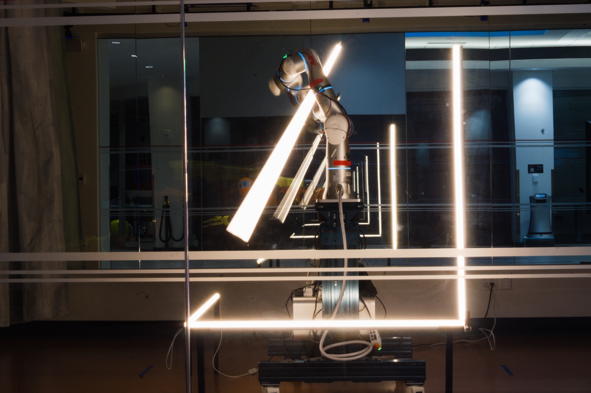 Robot arm holding a diagonal light tube reflected in a mirrored studio wall